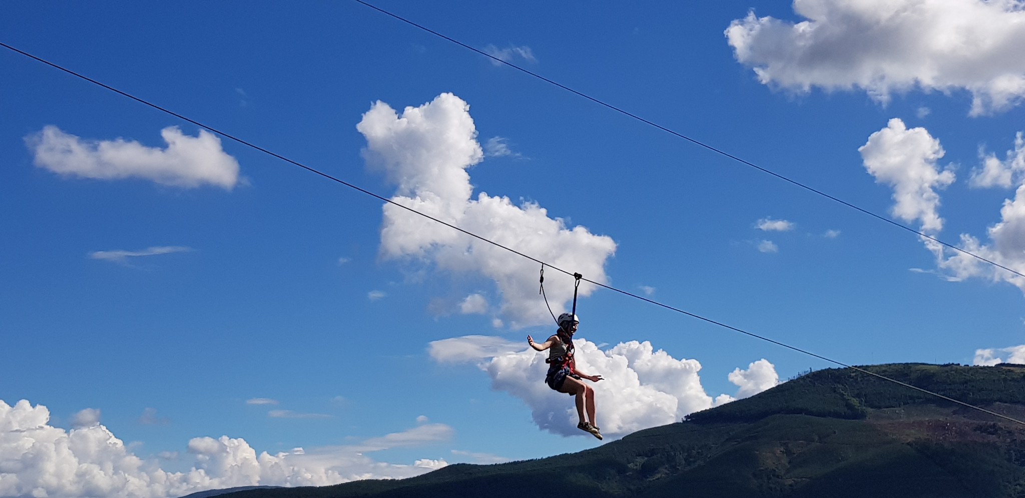 Jízda na zipline vysoko nad krajinou s horami a mraky v pozadí u Sudwaly