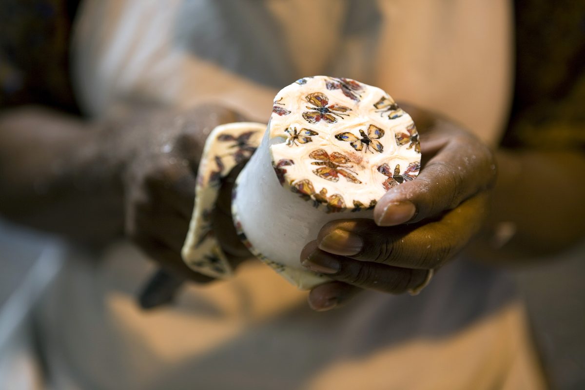 Close-up of an artisan's hands holding a finished candle decorated with a butterfly motif